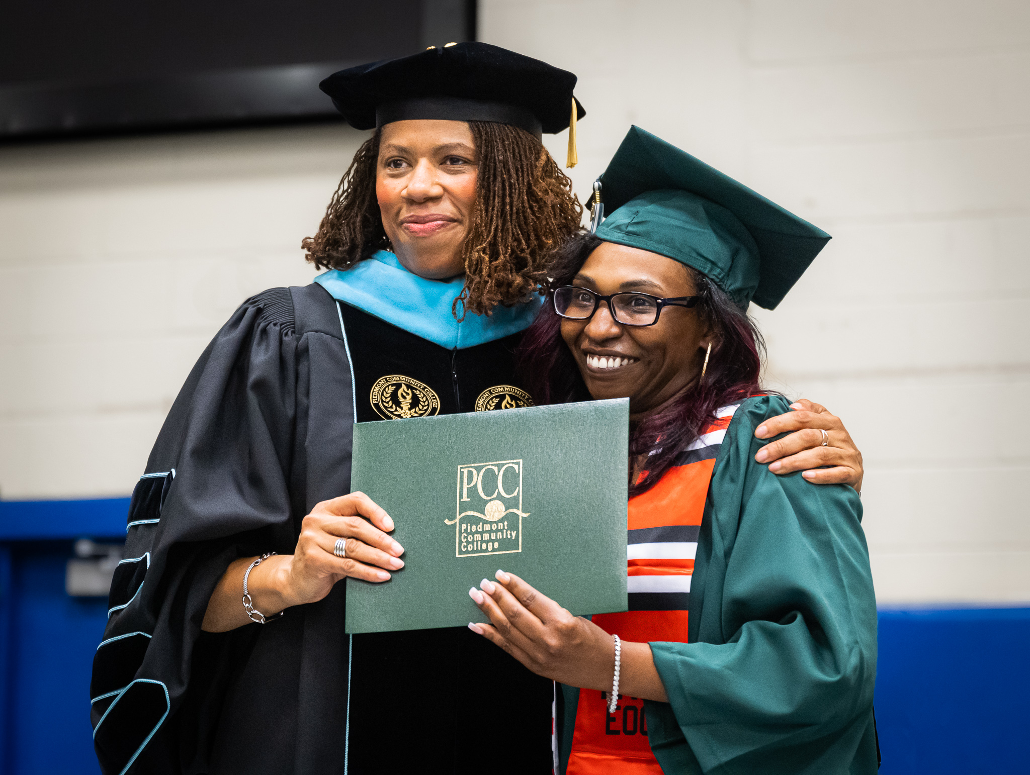 Dr. Senegal Poses with Graduate Terri Royster wearing graduate regalia while holding up diploma