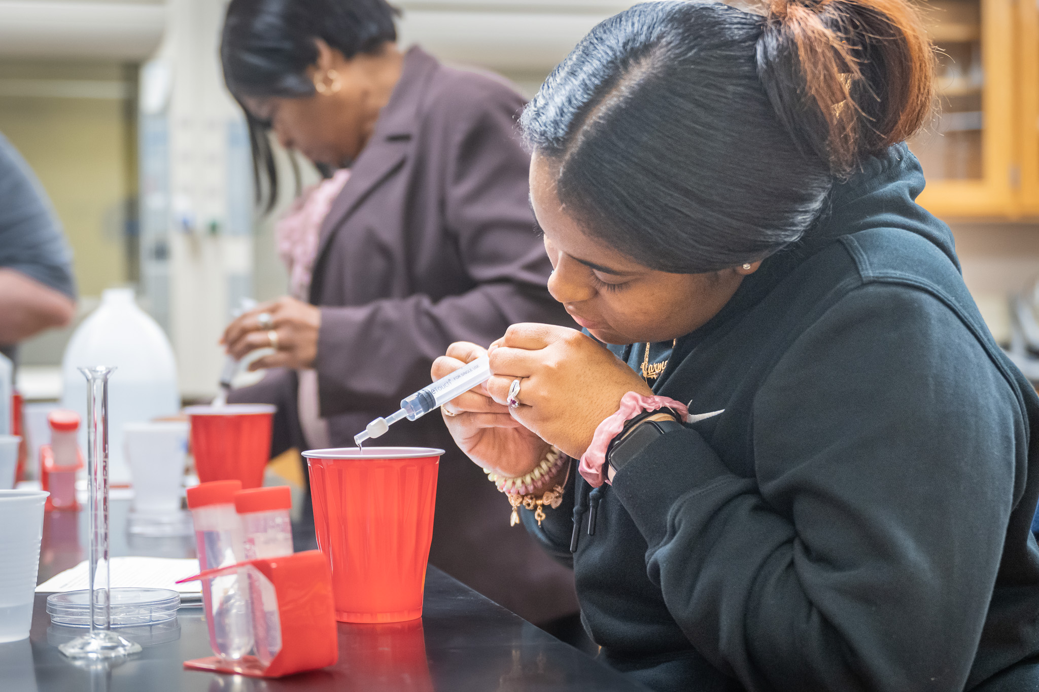 African American woman uses chemistry syringe to pour liquid into measuring device